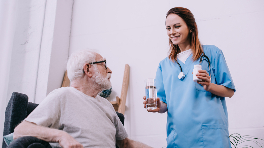 Krankenschwester gibt älterem Mann Medizin und Wasser