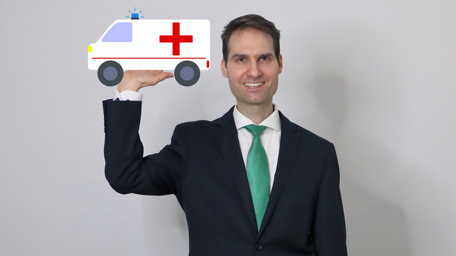 Ein Mann steht vor einer Wand und hält seinen linken Arm angewinkelt hoch. Auf der Handfläche ist ein gezeichneter Krankenwagen.