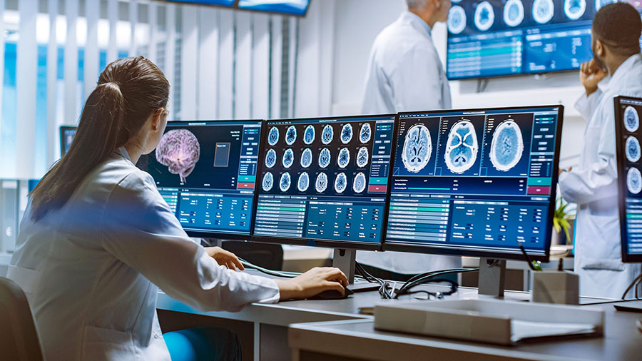 Ärztin betrachtet Monitore auf denen ein Gehirn abgebildet ist; © Adobe Stock